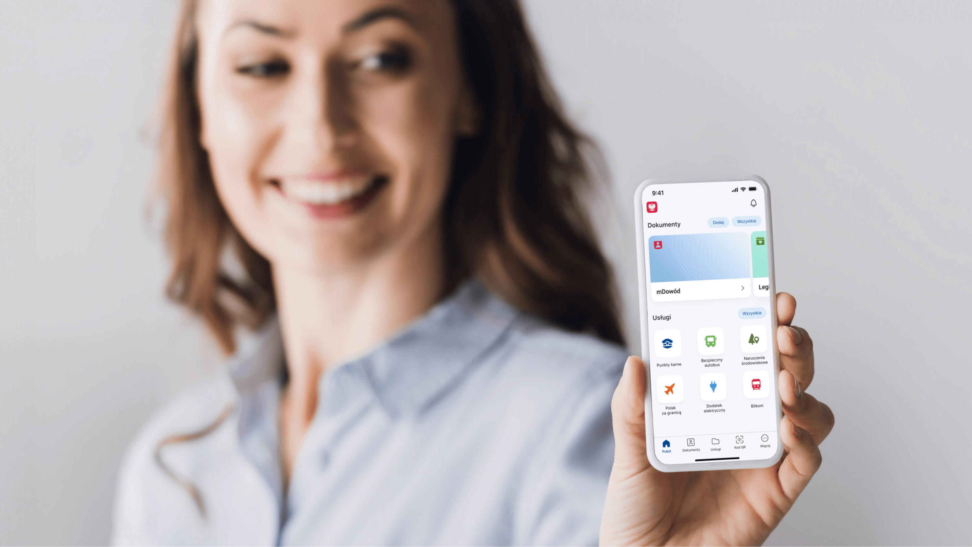 Kobieta pokazuje telefon, na którym pokazana jest aplikacja mobilna mObywatel