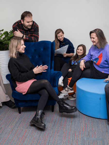Zespół Komunikacji - cztery kobiety i mężczyzna - rozmawia i śmieje się siedząc na pufach i fotelach w biurze COI